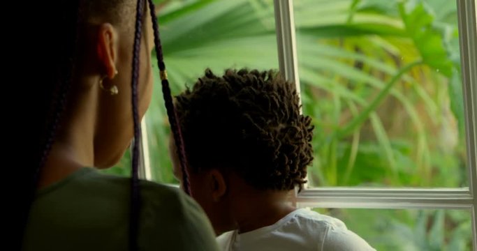 Rear view of young black mother playing with his son on window sill in a comfortable home 4k