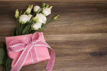 White flowers (eustoma) and a pink gift box with a pink rustic ribbon on a dark wooden background