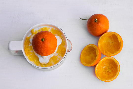 Vista cenital de un exprimidor blanco y varias naranjas ya exprimidas y una naranja entera