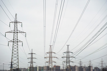 Power lines with many wires and metal supports on the open water against the sky. The concept of a modern city in the background and a lot of electrical wires in the foreground