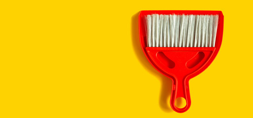 Red dustpan and brush lying on yellow background. In the style of pop art. Top view.