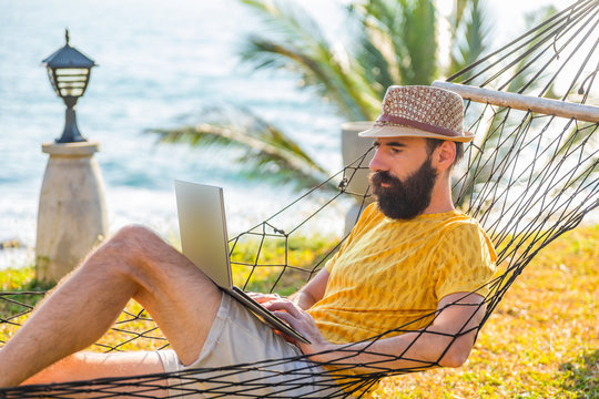 Man working with a laptop, on a hammock in the beach.
