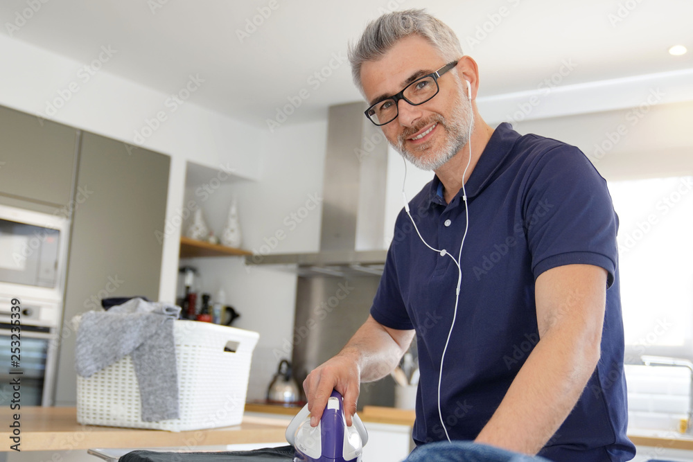 Poster Mature man ironing clean laundry at home