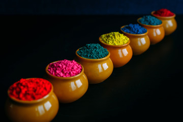 Line of colorful Holi powder in cups closeup. Bright colours for Indian holi festival in clay pots. Selective focus. Black background. Happy Holi greeting card