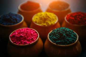 Colorful Holi powder in cups closeup. Bright colours for Indian holi festival in circle of clay pots. Selective focus. Black background