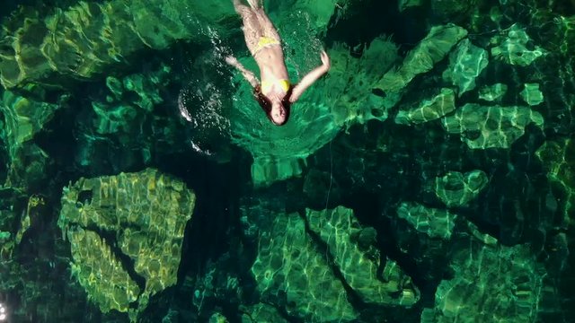 Young brunette woman floats and plays in a natural pool of a cenote in Mexico.