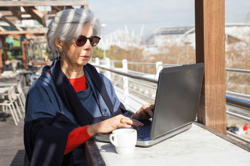 Serious senior lady working on computer in outdoor cafe