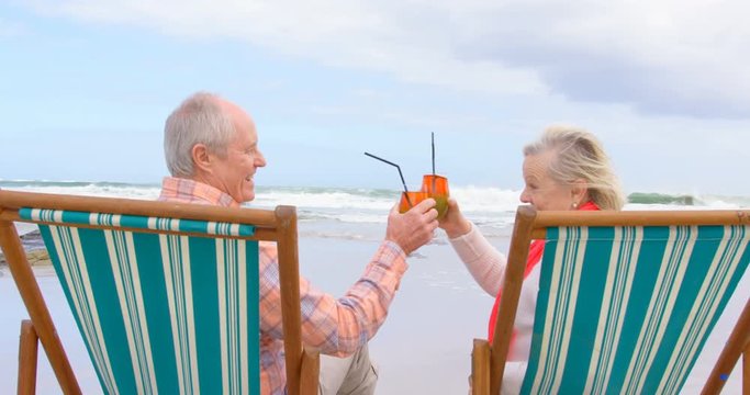 Side view of old caucasian senior couple toasting glasses of cocktail at beach 4k - Powered by Adobe