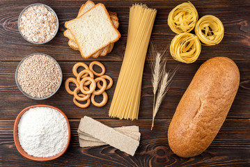 Fototapeta na wymiar Bakery and pasta products on dark wooden background. Baguette, pasta, dryings bagel, toast bread, crispbreads and bread.
