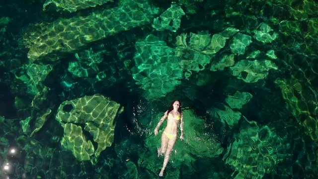 Young brunette woman floats and plays in a natural pool of a cenote in Mexico.