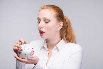Fototapeta na wymiar young red haired woman puts a coin into her piggy bank
