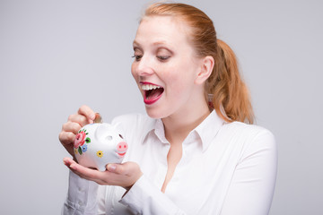 Fototapeta na wymiar young red haired and happy woman puts a coin into her piggy bank