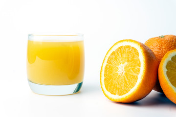Orange juice in a clear glass cup with fresh oranges.