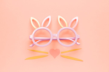 Bunny rabbit face made of colorful paper with sunglasses on bright background. Easter minimal concept. Flat lay. Living Coral color of the Year 2019.