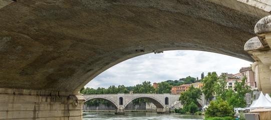 Italy, Rome, a bridge on the tiber river viewed below arch of another bridge