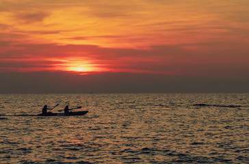 Naklejka premium Silhouette of couples are kayaking in the sea at sunset. Kayak in the tropical sea at sunset. Romantic couple travel on summer vacation. Adventure activities of romantic couples. Beautiful sunset sky