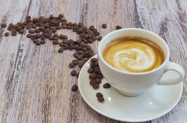 white cup with black coffee with milk. Handful of coffee beans on a wooden table. horizontal view of a cup with a coffee drink. Copy space close up.