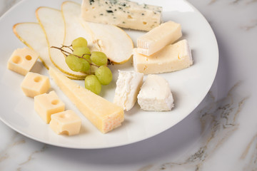 Käseteller mit Edamer, Parmesan, Blauschimmel Käse und Ziegenkäse an Birne und Trauben auf Teller und Marmor Hintergrund
