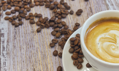 white cup with black coffee with milk. Handful of coffee beans on a wooden table. horizontal view of a cup with a coffee drink. Copy space close up.