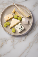 Käseteller mit Edamer, Parmesan, Blauschimmel Käse und Ziegenkäse an Birne und Trauben auf Teller und Marmor Hintergrund