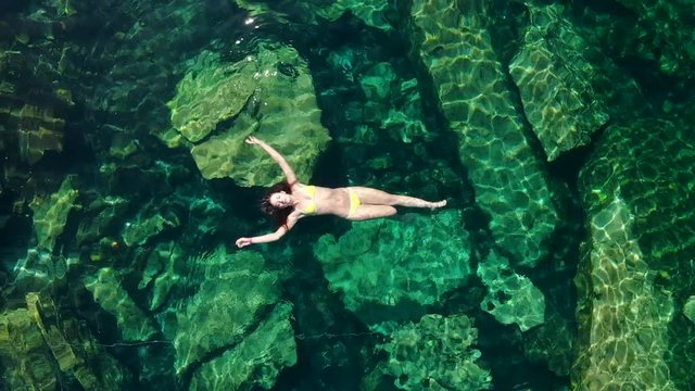 Young brunette woman floats and plays in a natural pool of a cenote in Mexico.