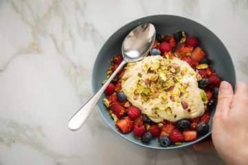 Frau isst Beeren Obstsalat mit Erdbeeren, Himbeeren, Blaubeeren, Pistazien, Zitronen Zesten, Leinöl Kurkuma Quark Creme in blauer Schale als Frühstück auf Marmor Hintergrund