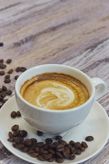 white cup with black coffee with milk. Handful of coffee beans on a wooden table. vertical view of drink with coffee. Copy space close up.
