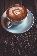 Latte art coffee with coffe beans on the table in vintage tone