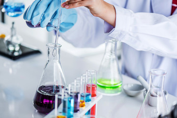 Scientist holding sampling oil or chemical liquid in flask with lab glassware in laboratory background, science or medical research and development concept  