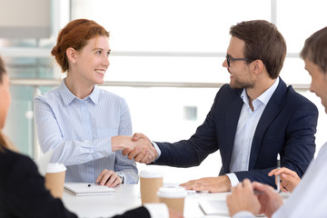 Millennial businesspeople gathered in boardroom starting negotiations shaking hands