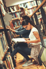 Two female students read and learns by the book shelf at the library.Reading a book.