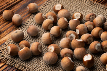 A pile of hazelnuts on a jute cloth and a wooden table made of aged burnt wood