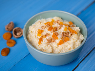 Millet porridge on a wooden blue table with nuts and dried fruits, dried apricots