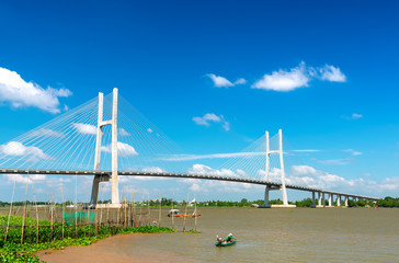 Fototapeta premium Dong Thap, Vietnam - January 17th, 2019: Fishermen are fishing in a small boat in the middle of the river, a cable-stayed bridge that represents the economic development in Dong Thap, Vietnam.