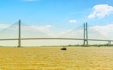 The small boat glides through the river beneath the newly completed giant cable stayed bridge showing the development of traffic in the Mekong Delta region of Vietnam.