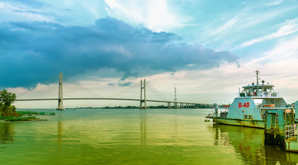 Fototapeta premium Dong Thap, Vietnam - January 16th, 2019: Landscape ferry about to leave port to transport passengers across Mekong river in spring, far away is Cao Lanh bridge just completed in Dong Thap, Vietnam.