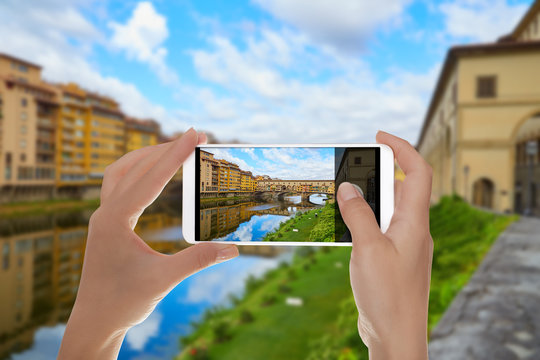 A man is making a photo of Ponte Vecchio Bridge in a summer sunny day without people on a mobile phone