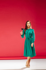 Studio shot of young beautiful woman on light background. Lady holding wineglass with wine while relaxing.