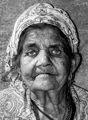 Close up portrait of old homeless Gypsy beggar woman with wrinkled face skin begging for money on the street in the city and looking in the camera with sad blue eyes vertical image black and white 