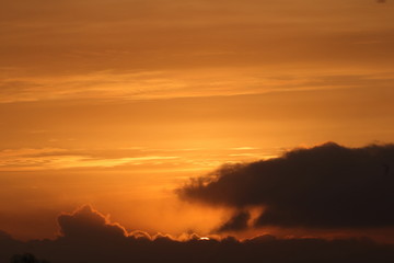 Fototapeta na wymiar Beautiful sun setting behind clouds, warm orange sky