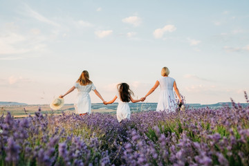 Fototapeta na wymiar Three girls holding hands are walking in a lavender field