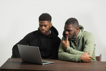 two sporty african men in tracksuits on a white background at a table with a laptop