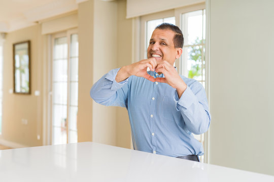 Middle age man sitting at home smiling in love showing heart symbol and shape with hands. Romantic concept.