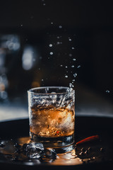 ice cube falls into a glass with a cocktail. coke, whiskey and ice. Fluid in motion. Droplets of spray.