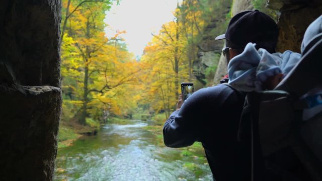 Male tourist with backpack taking pictures of the autumn scenery by smartphone 