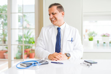 Middle age doctor man wearing medical coat at the clinic looking away to side with smile on face, natural expression. Laughing confident.