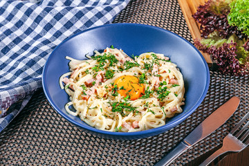Close up view on traditional homemade carbonara in blue bowl served on table. Italian cuisine with copy space. Useful pitcture for design or menu. Food flat lay