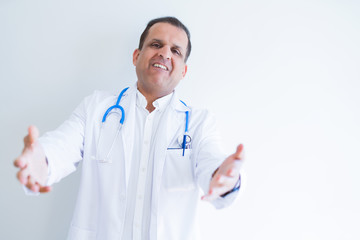 Middle age doctor man wearing stethoscope and medical coat over white background looking at the camera smiling with open arms for hug. Cheerful expression embracing happiness.