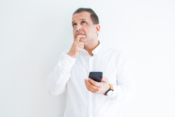 Middle age man using smartphone over white wall serious face thinking about question, very confused idea