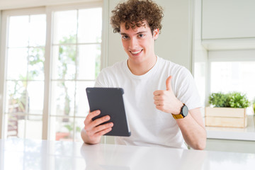 Young man using touchpad tablet happy with big smile doing ok sign, thumb up with fingers, excellent sign